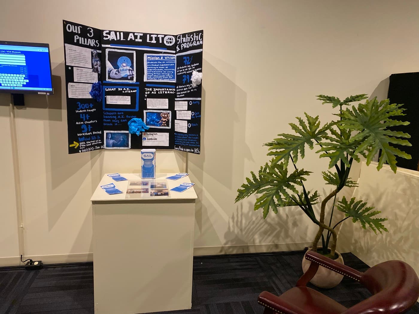The SAIL display in a museum gallery, with the poster board mounted above a plinth of brochures